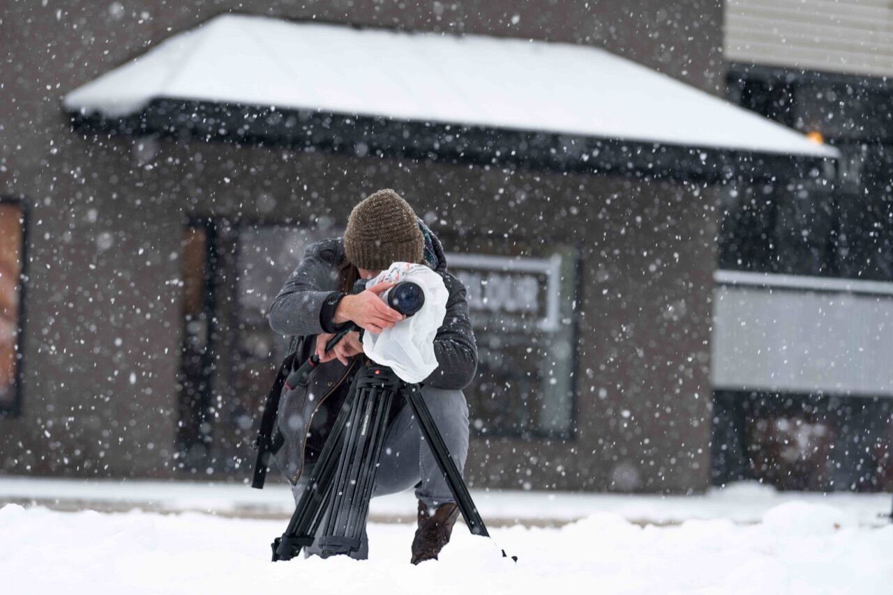 James Alton filming in falling snow in 2017, with a covered camera on a tripod.