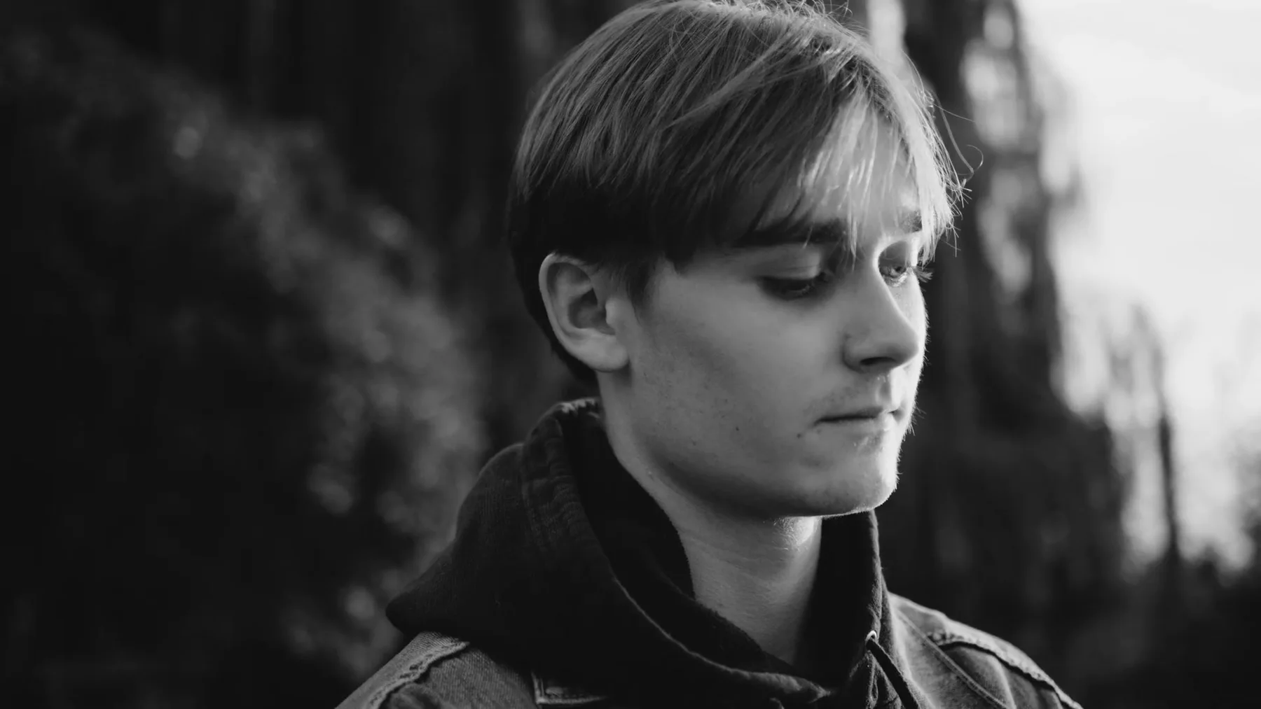 A young man looks down in a black-and-white outdoor frame.