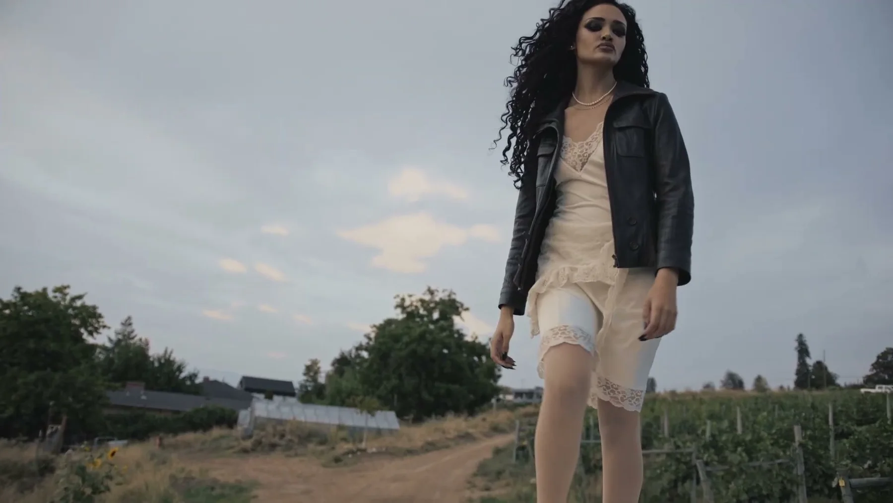 A woman in a dark jacket walks through a dry field.