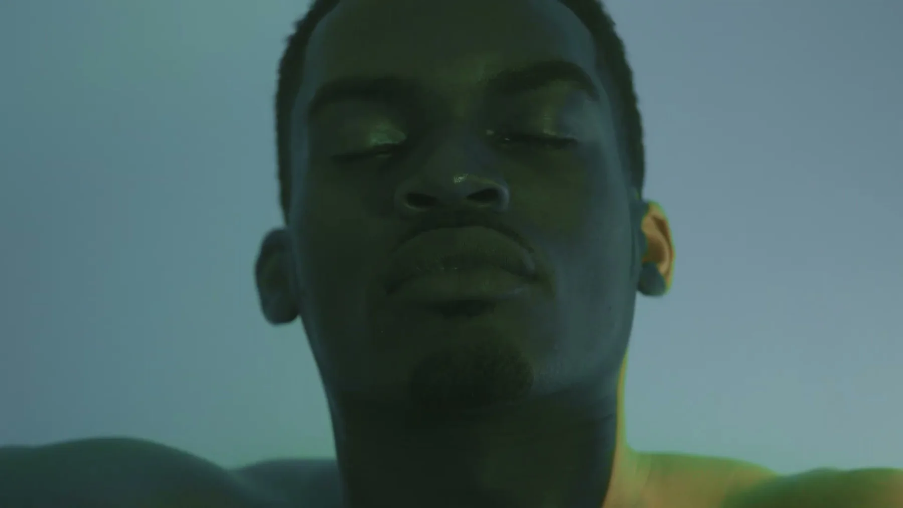 A man floats with his face above green-lit water.