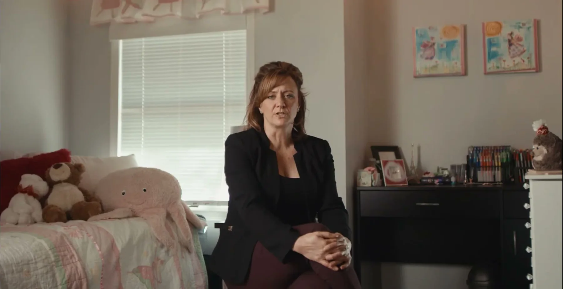 Ginny Becker speaks from a child-support bedroom with stuffed toys on the bed.