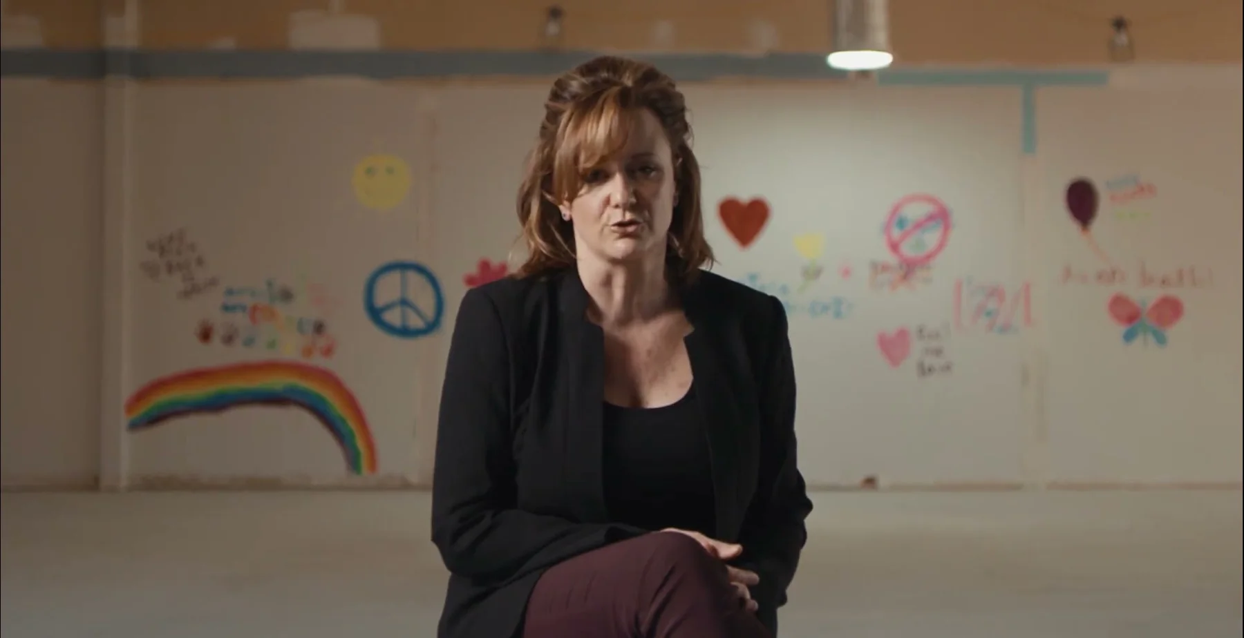 Ginny Becker speaks from a child-support room with drawings on the wall.