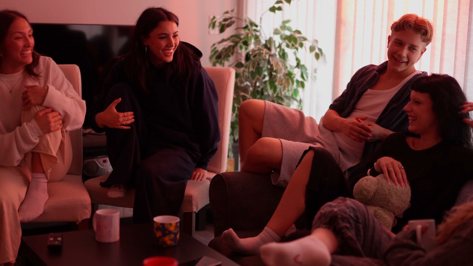 A group smiles together around a table in a pink-toned living-room scene from Jamie.