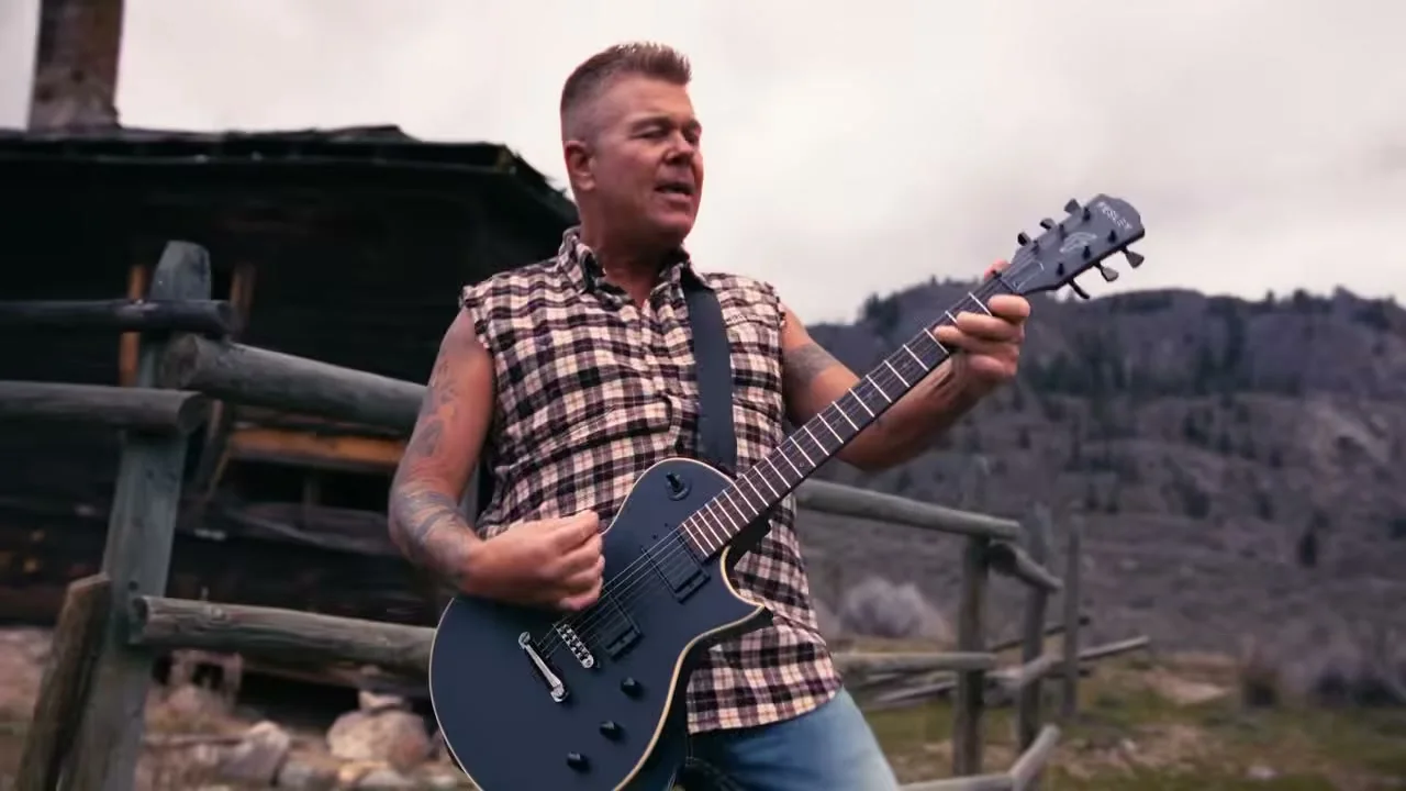 Trevor Ingram plays electric guitar outside a weathered wooden cabin in Nothing Down That Road.