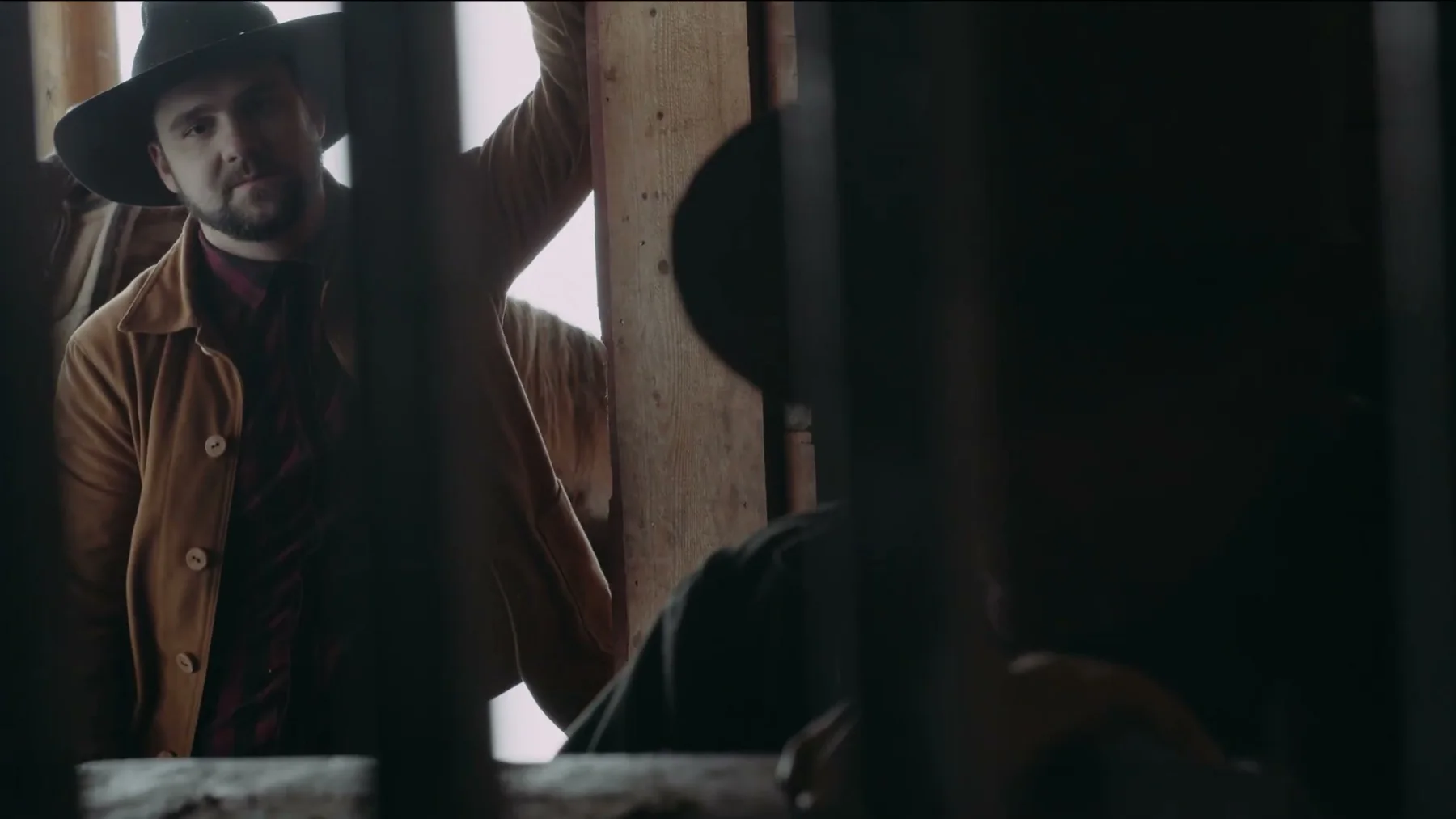 A younger man in a cowboy hat stands in a stable doorway.
