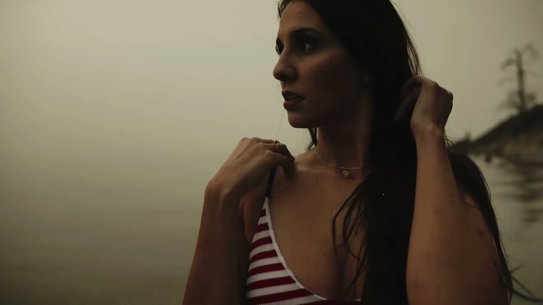 A woman stands beside the lake with wet hair and a striped top.