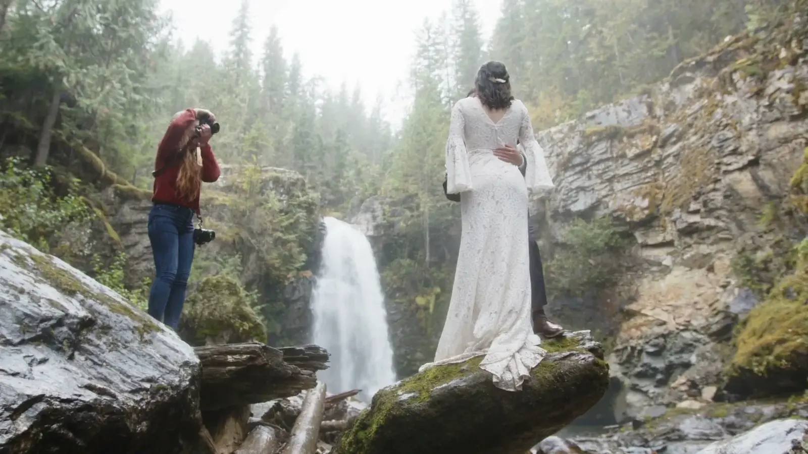 A photographer photographs a bride beside a waterfall.