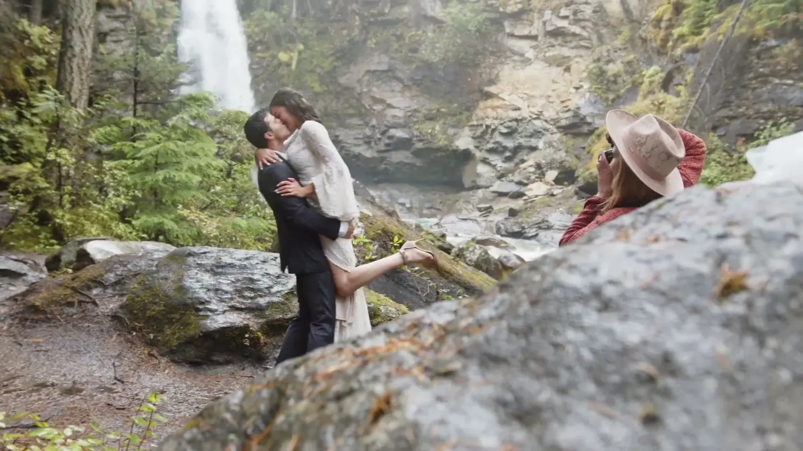 A photographer photographs a couple beside a waterfall.