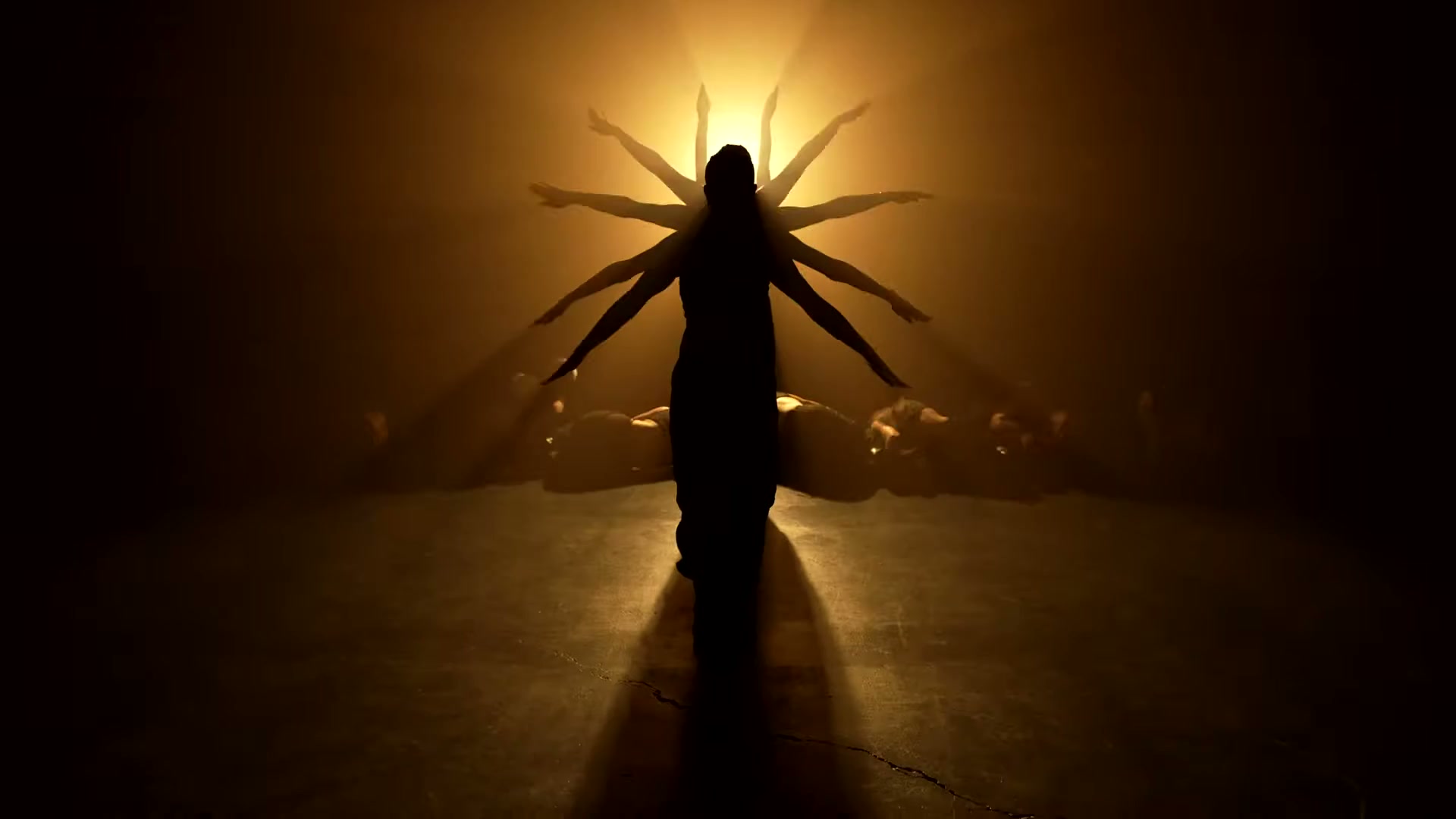 The Village Dance Academy's Sockeye ensemble forms a many-armed silhouette in amber backlight.