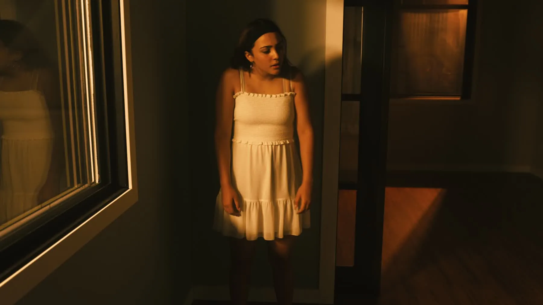 Dancer in a white dress standing near a window in Vienna Hank's choreography film.